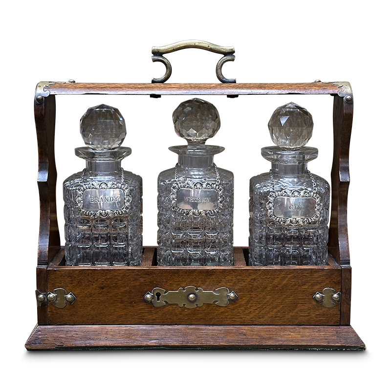 Victorian oak tantalus with 3 crystal decanters and brass mounts including sterling silver bottle labels