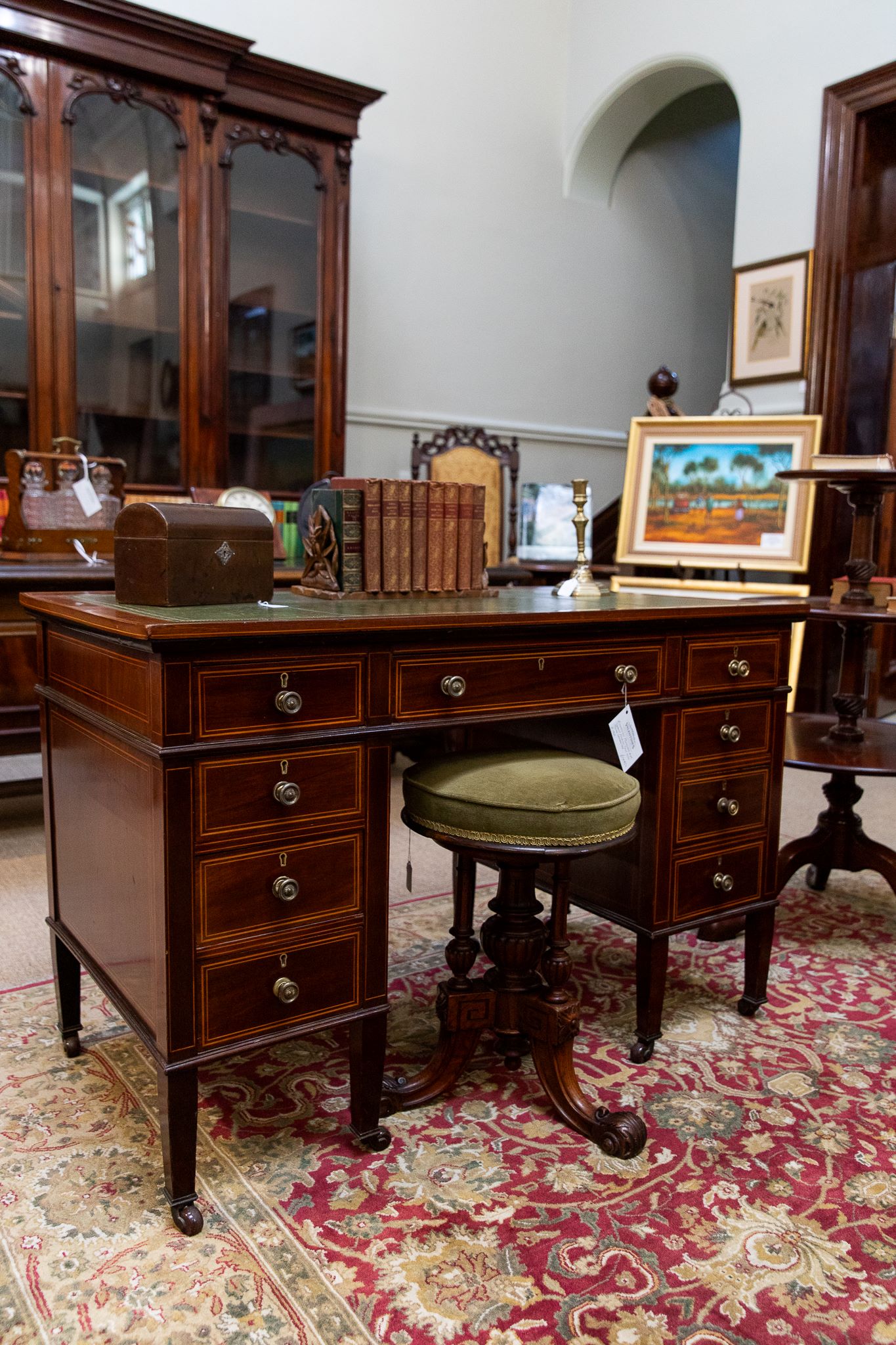 Antique desk with piano stool with art and antiques in the background